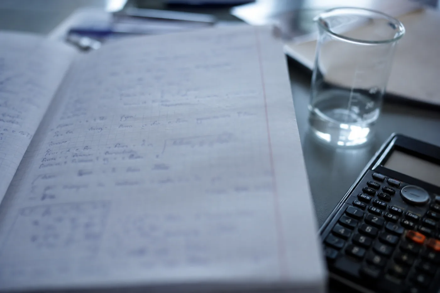 Un cahier de chimie ouvert avec une calculatrice scientifique et un b&eacute;cher